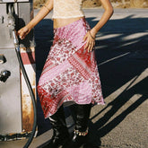 Person wearing a pink and red patterned skirt standing next to a gas pump.